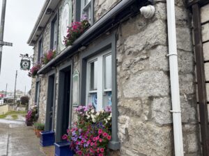 Stone pub exterior of Patrick Johnny Sally’s with flower boxes and hanging sign on a wet street