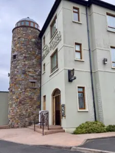 A stone tower is attached to a modern beige hotel building displaying “Glen Hotel & Lounge” signage. A Guinness pint glass sign hangs above the entrance, with a ramp and steps leading up to the welcoming pub door.