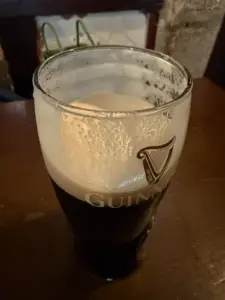 A partially full Guinness pint glass with a creamy head sits on a wooden table in a dimly lit pub.