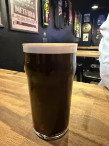 A Guinness pint glass sits on a wooden bar counter in a dimly lit pub decorated with music posters and band t-shirts on the walls.