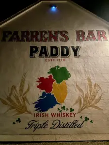 A mural on a building reads "Farren's Bar," "Paddy," "Est. 1779," with a map of Ireland in red, green, yellow, and blue, featuring a Guinness pint glass below “Irish Whiskey Triple Distilled,” all decorated with shamrocks and wheat.