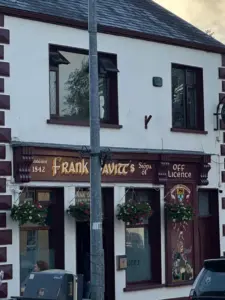 A pub called "Frank Lavitt's" with hanging flower baskets and a mural outside. A streetlight pole stands in front of the entrance. The building has white walls with maroon trim.