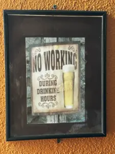 Framed sign on an orange wall that reads "NO WORKING DURING DRINKING HOURS" with an image of a Guinness pint glass beside the text, giving a playful pub vibe.