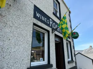 A stone building with a sign reading “WINES ROARTY,” green and yellow checkered flags, a Heineken sign above the entrance, and a Guinness pint glass displayed outside, all under a blue sky—classic pub charm.