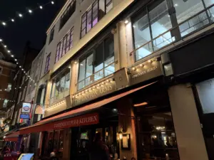 Nighttime street view of "The Canton Arms" pub, warm lights glowing and string lights above. A Guinness pint glass sits on a table beneath the red awning labeled "INDEPENDENT PUB & KITCHEN." The scene is lively and inviting.