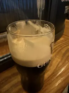 A partially drunk Guinness pint glass sits on a wooden pub counter, with foam clinging to the inside of the glass.