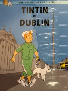 A comic-style illustration shows Tintin in a green tracksuit, walking his dog Snowy past Dublin's General Post Office; the Spire and a yellow bus are in the background. A Guinness pint glass sits outside a pub. The title reads "Tintin in Dublin.