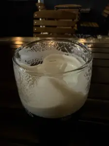 A half-full Guinness pint glass with foam residue on the rim sits on a wooden table, with blurred wooden chairs in the background in a dimly lit pub setting.