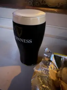 A pint of Guinness stout with a creamy head sits on a bar next to an open bag of potato chips.