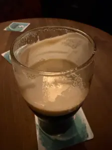 A partially finished pint of stout beer sits on a coaster atop a wooden table, with another coaster visible in the background.