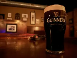 A pint of Guinness stout sits on a polished wooden bar in a dimly lit pub, with framed pictures from The Snug in Maine blurred in the background.
