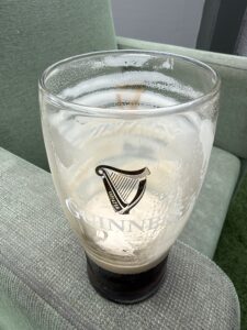 A nearly empty pint glass with a Guinness logo sits on a light green cushioned chair, with some foam clinging to the sides of the glass.