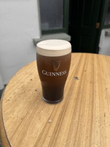 A pint of Guinness stout with a creamy head sits on a round wooden table, with a green door and white walls in the background.