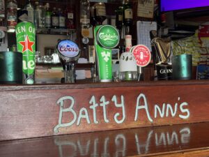 Beer taps for Heineken, Coors, Carlsberg, Smithwick’s, and Guinness on a bar counter with “Batty Ann’s” written on the front at an Irish pub.