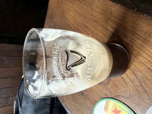 Guinness pint glass at The Widow’s (Belturbet), with foam residue and dark stout remaining on a wooden pub table