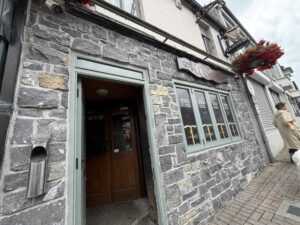 Exterior of The Widow’s pub in Belturbet, with Guinness sign, stone facade, and hanging flower basket